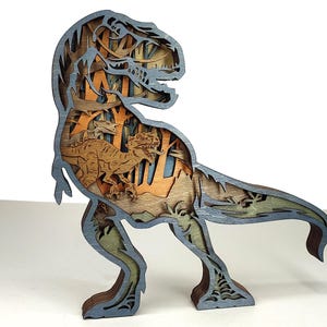Peut inclure: Sculpture en bois multicouche représentant un Tyrannosaurus Rex. Le dinosaure est principalement bleu-gris, avec un intérieur détaillé montrant une scène de forêt et d'autres dinosaures dans des tons bruns et orangés. La sculpture est autoportante.