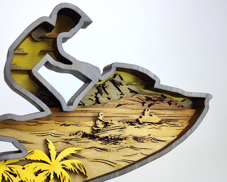 Pu&ograve; includere: Scultura in legno multistrato raffigurante una persona che fa jet ski. La scultura presenta un cielo giallo, acqua marrone e una palma gialla. Il pilota di jet ski &egrave; grigio e la scultura ha un bordo grigio.