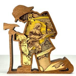 May include: A layered wooden sculpture depicting a firefighter kneeling, holding an axe. The artwork features a detailed interior scene with a building and another firefighter. The sculpture is primarily brown with yellow and gray accents.