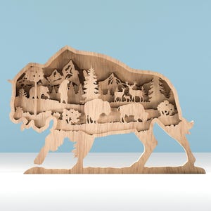 Könnte beinhalten: Ein hölzernes Kunstwerk in Form eines Bisons mit einem geschichteten Design. Das Innere zeigt eine Bergkette, Bäume und Wildtiersilhouetten, darunter Bären, Hirsche und andere Bisons. Das Stück ist aus hellem Holz gefertigt.