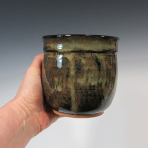 May include: A brown and green ceramic mug with a speckled glaze. The mug has a rounded shape and a slightly flared lip.