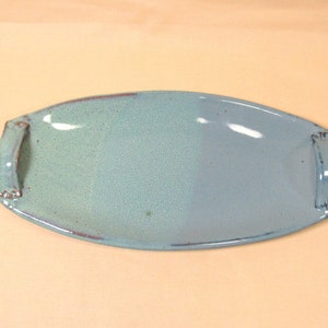 May include: A light blue ceramic serving tray with two handles. The tray has a light blue glaze with a subtle speckled texture.