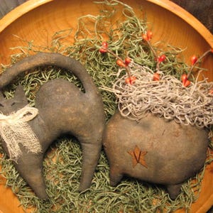 Op de afbeelding: Een rustieke houten kom bevat een zwart kattenbeeldje met een jute strik en een ketelvormige decoratie. De ketel heeft een ster en is gevuld met gedroogd mos en rode bessen, wat een Halloween-thema oproept.