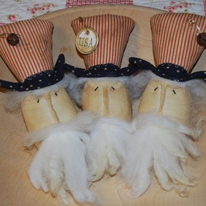 May include: Three handmade patriotic figures with red, white and blue striped hats, black and white star-shaped bands, and white beards. The hats have a small bell and a tag that says "USA".
