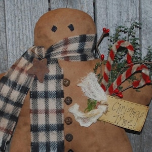 May include: A gingerbread man decoration with a plaid scarf and star detail. It has button features and holds candy canes and greenery. A tag reads "Christmas Time!"