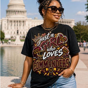 May include: A black short-sleeve t-shirt featuring a graphic print with the text "just a GIRL who LOVES HER COMMANDERS". The design includes a football helmet, a football, a crown, hearts, and a bow, all in burgundy, gold, and white colors.