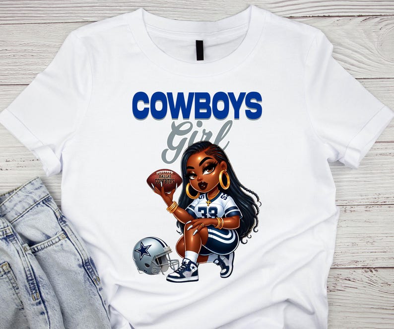 Pu&ograve; includere: T-shirt bianca con un'illustrazione a cartoni animati di una donna inginocchiata che tiene un pallone da football. La scritta "COWBOYS Girl" &egrave; in blu e grigio. &Egrave; visibile anche un casco da football.