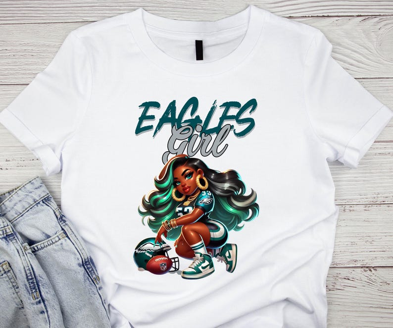 Pu&ograve; includere: T-shirt bianca con un'illustrazione a cartoni animati di una donna in uniforme da football, con la scritta "EAGLES GIRL" in verde acqua e argento. La donna &egrave; inginocchiata accanto a un pallone da football e a un casco, con dettagli verdi e neri.