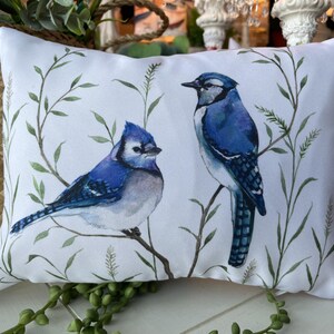 Peut inclure: Coussin rectangulaire blanc avec une illustration à l'aquarelle de deux geais bleus perchés sur une branche avec des feuilles vertes. Les oiseaux ont des plumes bleues, noires et blanches. Un accessoire de décoration.
