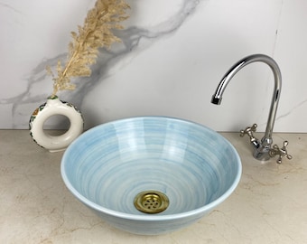 Op de afbeelding: Een lichtblauwe keramische badkamer wastafel met een swirl-patroon. De wastafel heeft een messing afvoer en wordt getoond met een chromen kraan.