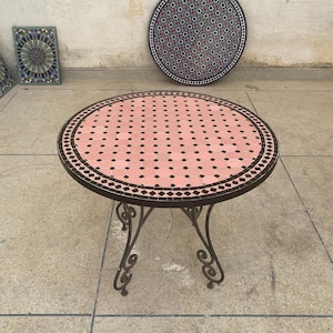 May include: A round, pink and black mosaic tile table with a wrought iron base. The table top has a repeating diamond pattern.
