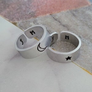 Peut inclure: Deux bagues en argent avec les initiales "J" et "M" gravées dessus. L'une a un motif de croissant de lune et l'autre a un motif d'étoile.