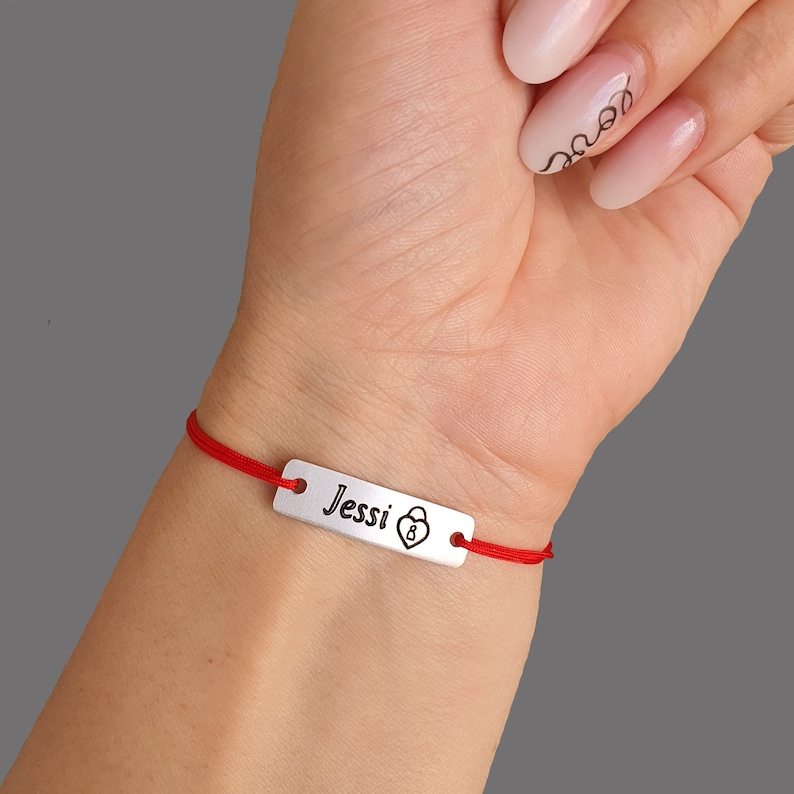 May include: Red string bracelet with a silver charm that says "Jessi" with a heart and lock symbol.