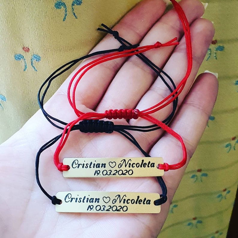 Pu&ograve; includere: Due braccialetti personalizzati con targhette rettangolari color oro. Ogni targhetta riporta i nomi "Cristian ♡ Nicoleta" e la data "19.03.2020" incisi. Un braccialetto ha un cordino rosso, l'altro nero.