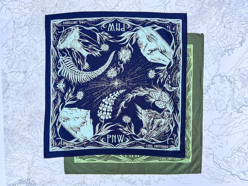 May include: A navy blue bandana with a white and light blue design featuring a fern, a mountain, and the text "PNW" repeated. The bandana is folded and layered on top of a green bandana.