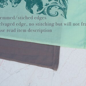 May include: A light green fabric square with a dark green floral design and a bear illustration. The fabric has 3 hemmed/stitched edges and 1 selvaged edge. The text "3 Hemmed/stitched edges 1 Selvaged edge, no stitching but will not fray, Please read item description" is printed on the fabric.
