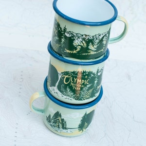 May include: Three stacked enamel mugs with a green and blue design featuring a mountain scene and the text "Olympic National Park".