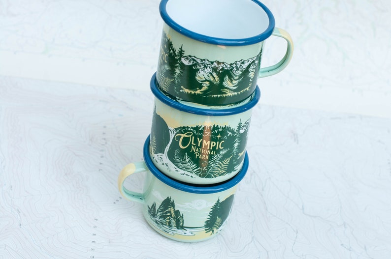 May include: Three stacked enamel mugs with a green and blue design featuring a mountain scene and the text "Olympic National Park".
