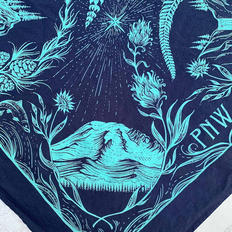 May include: A blue bandana featuring a mountain range, a star, and floral designs. The text "PNW" is printed in the bottom right corner.