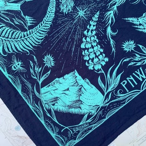 May include: A blue bandana featuring a mountain range, a star, and a fern design. The bandana has the text "PNW" in white lettering.