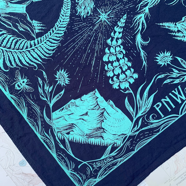 May include: A blue bandana featuring a mountain range, a star, and a fern design. The bandana has the text "PNW" in white lettering.