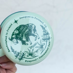 May include: A green enamel mug with a white goat illustration and the text "Final Witchback" and "Handcrafted in Poland". The mug also has the text "Designed in Portland, OR" and "Fireproof + Dishwasher Safe".
