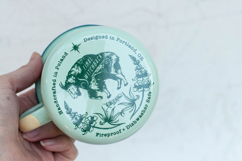 May include: A green enamel mug with a white goat illustration and the text "Final Witchback" and "Handcrafted in Poland". The mug also has the text "Designed in Portland, OR" and "Fireproof + Dishwasher Safe".