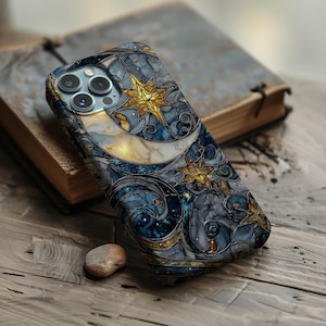 May include: A smartphone case with a stained-glass design featuring a crescent moon and stars in shades of blue, gold, and white. The case is lying on a wooden surface next to a book.