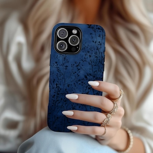 Könnte beinhalten: Eine dunkelblaue Smartphone-Hülle mit einem schwarzen Silhouettenmuster aus zarten Zweigen und kleinen Blättern. Die Hülle verfügt über eine Aussparung für ein Dreifach-Kamerasystem in der oberen linken Ecke und eine matte Oberfläche.