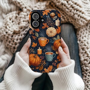 Op de afbeelding: Een telefoonhoesje met een herfstthema. Het toont pompoenen, herfstbladeren, koffiemokken, kaarsen en kaneelstokjes tegen een donkerblauwe achtergrond. Het ontwerp roept een gezellige, seizoensgebonden sfeer op.