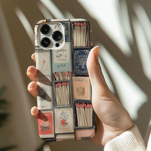 May include: A phone case with a colorful design featuring a grid of matchboxes with various labels and illustrations. The case is made of a hard plastic material and has a clear back.