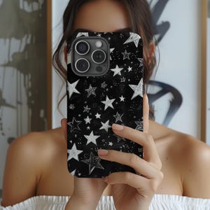 Pode incluir: Uma capa de telefone preta com um padr&atilde;o de estrelas brancas. A capa tem um recorte para a lente da c&acirc;mera e uma borda elevada ao redor das bordas.