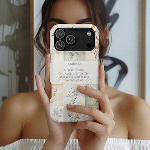 May include: A floral patterned phone case with a cream-colored background and a grid design. The case features a quote from Joshua 1:9: "BE STRONG AND COURAGEOUS, FOR THE LORD YOUR GOD IS WITH YOU WHEREVER YOU GO."
