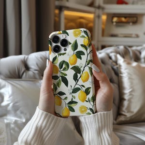 May include: A white phone case with a lemon print. The case has a white background with green leaves and yellow lemons. The phone case is designed for an iPhone.
