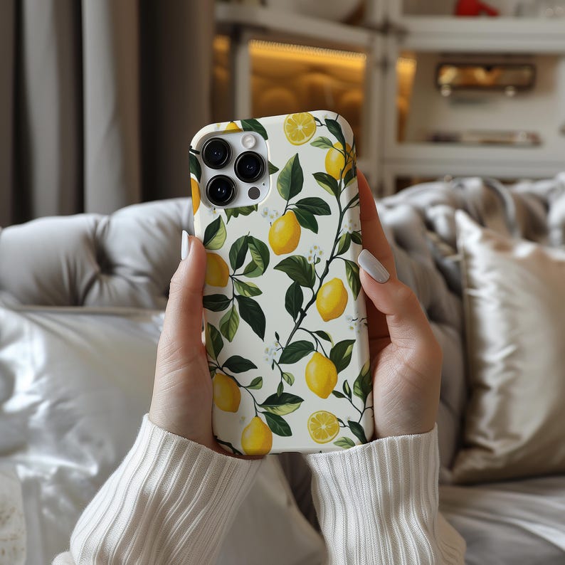 May include: A white phone case with a lemon print. The case has a white background with green leaves and yellow lemons. The phone case is designed for an iPhone.