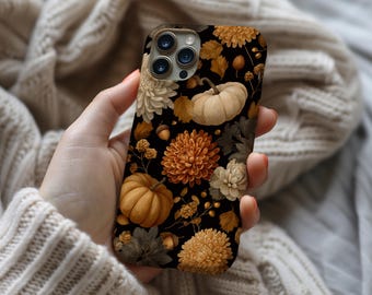 May include: A black phone case featuring a fall-themed design. The case is adorned with pumpkins, chrysanthemums, leaves, and acorns in shades of orange, cream, and brown. The floral and autumnal elements create a seasonal aesthetic.
