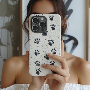 May include: A white phone case with a black paw print pattern. The case has a camera lens cutout and a white background.
