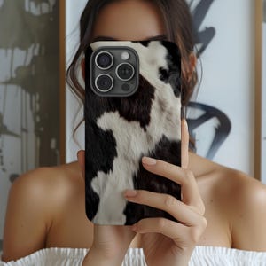 May include: A black and white cow print phone case for an iPhone.