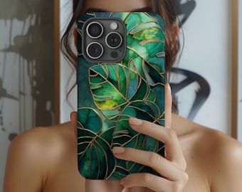 May include: A smartphone case featuring a vibrant green and gold leaf design. The case has a dark green background with gold outlines and accents, creating a tropical aesthetic. The phone case is held in front of a person.