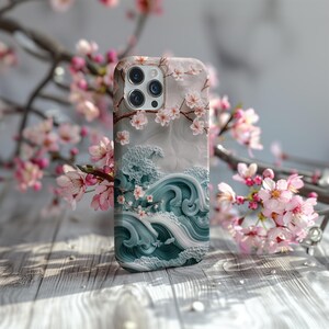 Może przedstawiać: Białe etui na iPhone z wzorem niebieskich fal i różowych kwiatów wiśni. Etui ma wycięcie na obiektyw aparatu i białe tło.