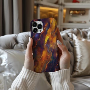 May include: A phone case with a colorful abstract design featuring shades of orange, yellow, and purple. The case has a camera cutout and a sleek, modern design.