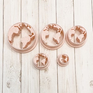 May include: Four pink plastic cookie cutters shaped like the Earth, in various sizes.