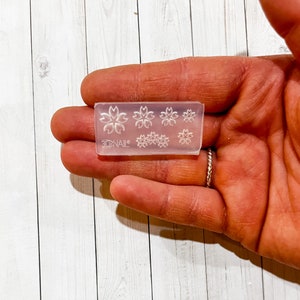 May include: A clear, rectangular nail art stamper with multiple flower designs. The stamper has six different flower patterns, including a larger flower design and smaller flower designs. The brand name "3DNAIL" is printed on the stamper.