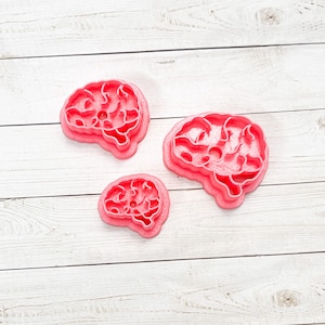 May include: Three pink plastic cookie cutters shaped like brains, of different sizes.