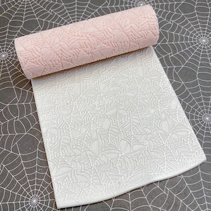 May include: A white silicone rolling pin with a spiderweb design. The rolling pin is rolled out on a white surface with a spiderweb design.