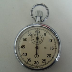Puede incluir: Un reloj de bolsillo plateado con una esfera blanca y agujas negras. El reloj tiene una esfera grande con números del 5 al 60, y una esfera más pequeña con números del 1 al 12. El reloj está hecho en la URSS.