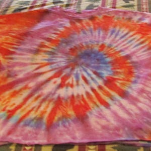 May include: A long-sleeved shirt with a tie-dye pattern in shades of pink, orange, and blue. The shirt has a spiral design.