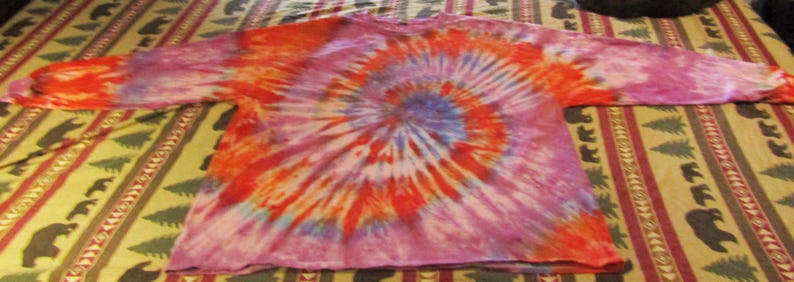 May include: A long-sleeved shirt with a tie-dye pattern in shades of pink, orange, and blue. The shirt has a spiral design.