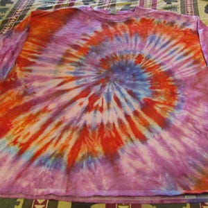 May include: A long-sleeved shirt with a tie-dye pattern in shades of purple, orange, red, and blue. The shirt has a spiral design.