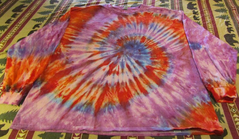 May include: A long-sleeved shirt with a tie-dye pattern in shades of purple, orange, red, and blue. The shirt has a spiral design.